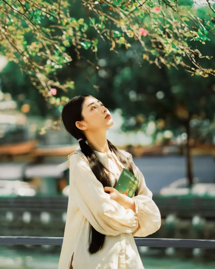 Cô gái ôm cuốn sách, ngước nhìn tán cây xanh