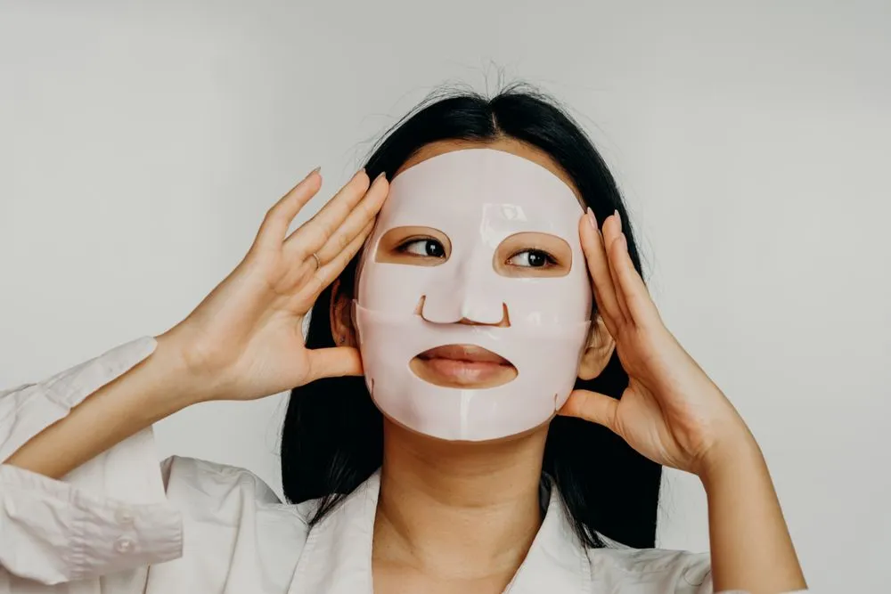 Cô gái đắp mặt nạ giấy dưỡng ẩm, hai tay áp lên má