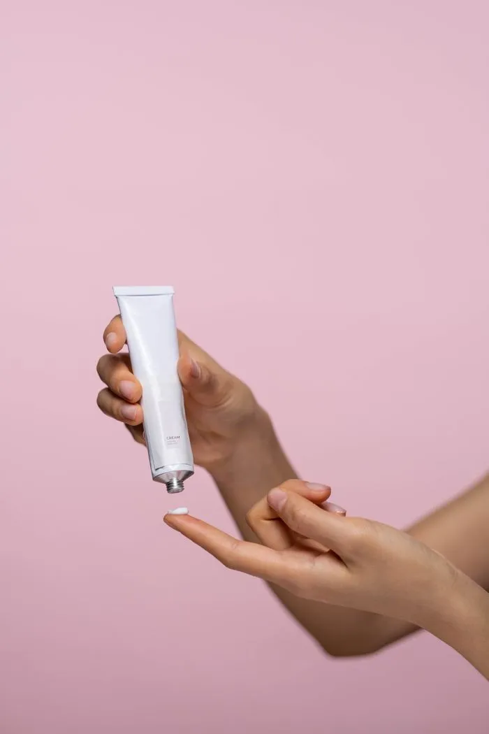 Bàn tay cầm tuýp kem trắng trước nền hồng